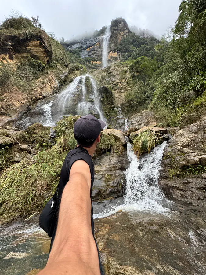 Persona señalando una cascada escalonada entre montañas