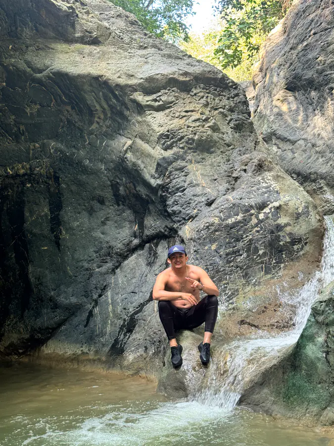 Hombre sonriente sentado junto a una cascada en la roca